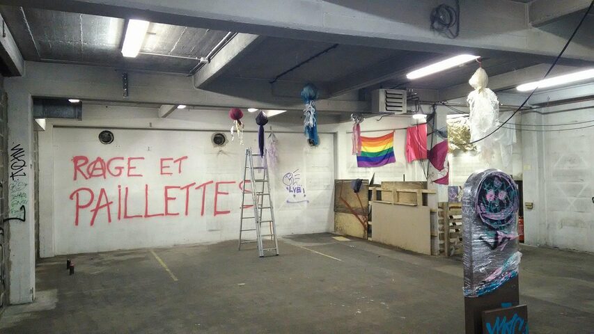 Une photo dans un bâtiment industriel avec des décorations queers et un tag "rage et paillettes"